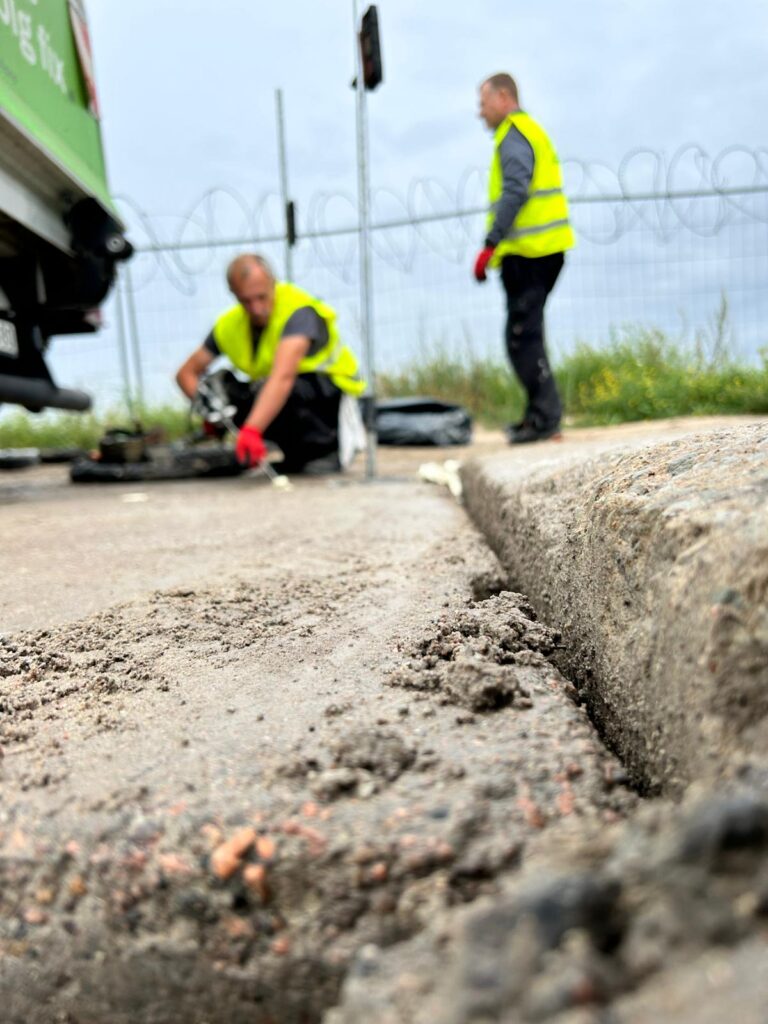 Workers performing geopolymer floor lifting injection to stabilize sinking concrete slab
