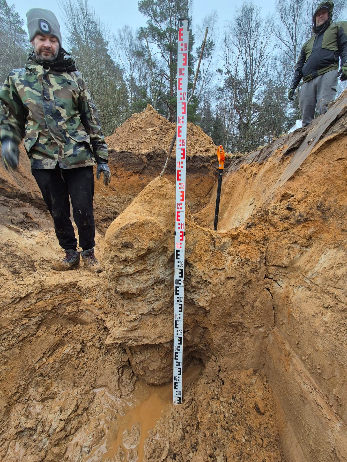 Bryła utwardzonego geopolimeru odkopana w gruncie piaszczystym, obok łata pomiarowa pokazująca jej wysokość