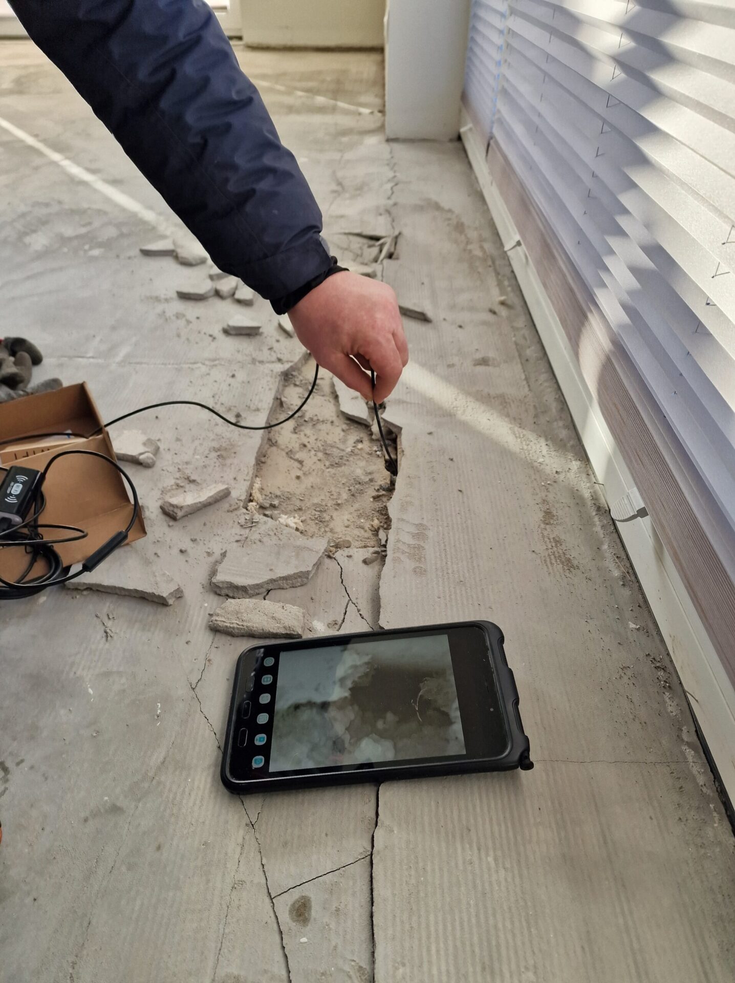 Kontrola przestrzeni pod pękniętą posadzką kamerą inspekcyjną, obraz widoczny na ekranie tabletu
